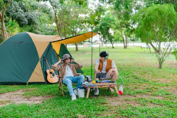 İki Asyalı erkek arkadaş gölün kenarında dinleniyor, müziğin tadını çıkarıyor ve açık hava ortamında birlikte şarkı söylüyorlar. Sahne, kamp gezisi sırasında neşeli ve huzurlu bir bağ ve yaratıcılık anı yakalıyor.