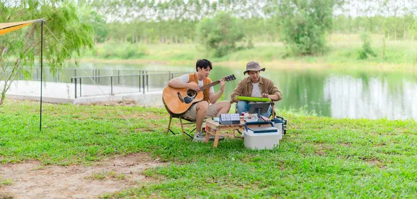 İki Asyalı erkek arkadaş gölün kenarında dinleniyor, müziğin tadını çıkarıyor ve açık hava ortamında birlikte şarkı söylüyorlar. Sahne, kamp gezisi sırasında neşeli ve huzurlu bir bağ ve yaratıcılık anı yakalıyor.