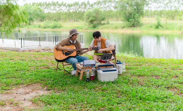 İki Asyalı erkek arkadaş gölün kenarında dinleniyor, müziğin tadını çıkarıyor ve açık hava ortamında birlikte şarkı söylüyorlar. Sahne, kamp gezisi sırasında neşeli ve huzurlu bir bağ ve yaratıcılık anı yakalıyor.