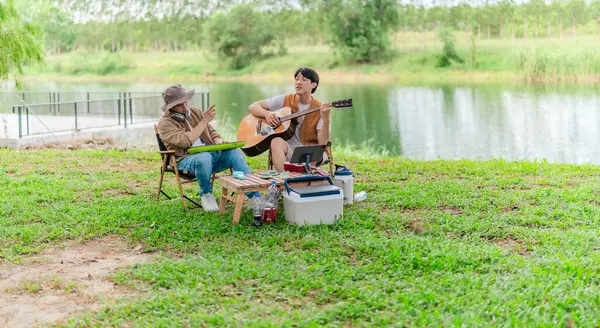 İki Asyalı erkek arkadaş gölün kenarında dinleniyor, müziğin tadını çıkarıyor ve açık hava ortamında birlikte şarkı söylüyorlar. Sahne, kamp gezisi sırasında neşeli ve huzurlu bir bağ ve yaratıcılık anı yakalıyor.