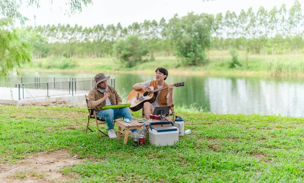 İki Asyalı erkek arkadaş gölün kenarında dinleniyor, müziğin tadını çıkarıyor ve açık hava ortamında birlikte şarkı söylüyorlar. Sahne, kamp gezisi sırasında neşeli ve huzurlu bir bağ ve yaratıcılık anı yakalıyor.
