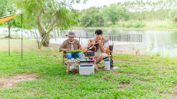 İki Asyalı erkek arkadaş gölün kenarında dinleniyor, müziğin tadını çıkarıyor ve açık hava ortamında birlikte şarkı söylüyorlar. Sahne, kamp gezisi sırasında neşeli ve huzurlu bir bağ ve yaratıcılık anı yakalıyor.