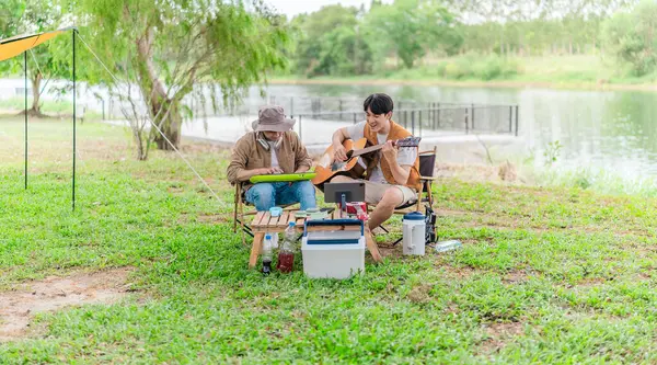 İki Asyalı erkek arkadaş gölün kenarında dinleniyor, müziğin tadını çıkarıyor ve açık hava ortamında birlikte şarkı söylüyorlar. Sahne, kamp gezisi sırasında neşeli ve huzurlu bir bağ ve yaratıcılık anı yakalıyor.