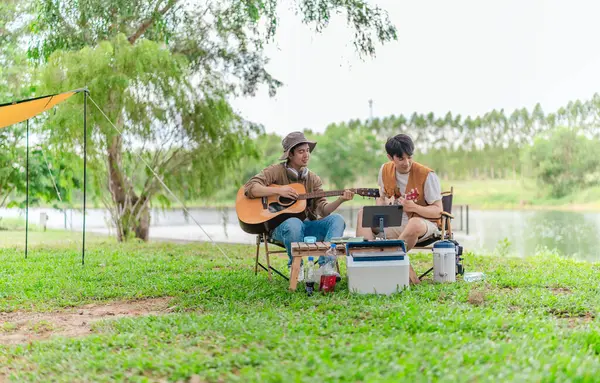 İki Asyalı erkek arkadaş gölün kenarında dinleniyor, müziğin tadını çıkarıyor ve açık hava ortamında birlikte şarkı söylüyorlar. Sahne, kamp gezisi sırasında neşeli ve huzurlu bir bağ ve yaratıcılık anı yakalıyor.