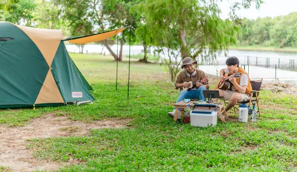 İki Asyalı erkek arkadaş gölün kenarında dinleniyor, müziğin tadını çıkarıyor ve açık hava ortamında birlikte şarkı söylüyorlar. Sahne, kamp gezisi sırasında neşeli ve huzurlu bir bağ ve yaratıcılık anı yakalıyor.