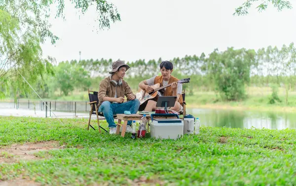 İki Asyalı erkek arkadaş gölün kenarında dinleniyor, müziğin tadını çıkarıyor ve açık hava ortamında birlikte şarkı söylüyorlar. Sahne, kamp gezisi sırasında neşeli ve huzurlu bir bağ ve yaratıcılık anı yakalıyor.