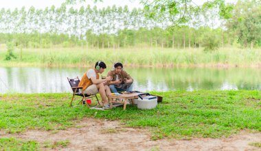 İki genç Asyalı erkek, kamp alanında dinlenirken tablet üzerinde video oyunu oynamaktan hoşlanırlar. Kamp malzemeleri, gitarlar ve doğa ile çevrili sahne, modern ve neşeli doğa deneyimini yakalar..