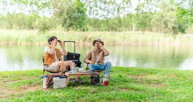 İki Asyalı erkek arkadaş, doğa ve teçhizatla çevrili bir gölün kenarında sakin bir kamp deneyimi yaşıyor. Sahne, rahatlamış bir doğa keşfi anı yakalıyor ve manzaralı bir ortamda hazırlanıyor..