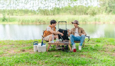 İki Asyalı erkek arkadaş, doğa ve teçhizatla çevrili bir gölün kenarında sakin bir kamp deneyimi yaşıyor. Sahne, rahatlamış bir doğa keşfi anı yakalıyor ve manzaralı bir ortamda hazırlanıyor..