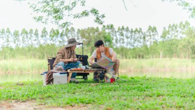 İki Asyalı erkek arkadaş, doğa ve teçhizatla çevrili bir gölün kenarında sakin bir kamp deneyimi yaşıyor. Sahne, rahatlamış bir doğa keşfi anı yakalıyor ve manzaralı bir ortamda hazırlanıyor..
