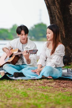 Asyalı bir çift göl kenarında barışçıl bir pikniğin keyfini çıkarırken, akustik gitar çalan bir adam da birbirlerine sıcak bir şekilde bağlanıyorlar. Doğal ortamdaki romantik ve müzikal bir an..