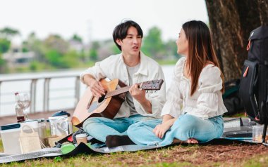 Asyalı bir çift göl kenarında barışçıl bir pikniğin keyfini çıkarırken, akustik gitar çalan bir adam da birbirlerine sıcak bir şekilde bağlanıyorlar. Doğal ortamdaki romantik ve müzikal bir an..