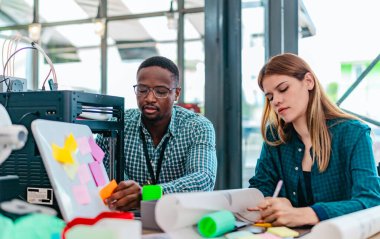 Girişimci profesyonellerden oluşan çeşitli bir ekip, modern bir çalışma alanında üç boyutlu bir baskı projesi üzerinde işbirliği yapmaktadır. Yaratıcı bir teknoloji ortamında yenilik, takım çalışması ve prototipleme sürecinin altını çizmek.