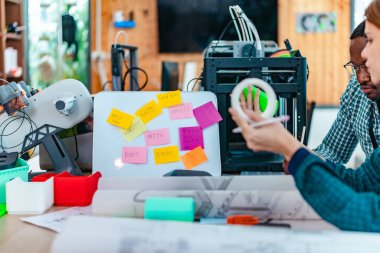 Girişimci profesyonellerden oluşan çeşitli bir ekip, modern bir çalışma alanında üç boyutlu bir baskı projesi üzerinde işbirliği yapmaktadır. Yaratıcı bir teknoloji ortamında yenilik, takım çalışması ve prototipleme sürecinin altını çizmek.