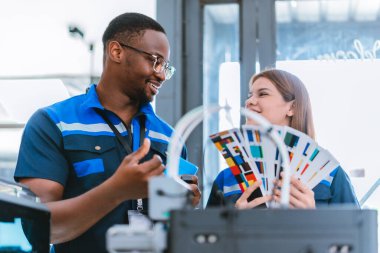 3D yazıcının yanında dikilirken mühendisler renk örnekleme kılavuzunu gözden geçirir, geri dönüşümlü 3D yazdırılmış ürünler için renk seçerler. Üretim süreçlerinde yaratıcılık, sürdürülebilirlik ve kesinliğin vurgulanması