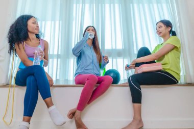 Çeşitli bayan arkadaş grupları antrenmandan sonra birlikte rahatlar, susuzluk çeker ve sohbet ederler. Yoga bloğu, direnç bandı ve egzersiz topuyla çevrili. Sağlıklı yaşam, dostluk, sağlıklı yaşam.