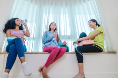 Çeşitli bayan arkadaş grupları antrenmandan sonra birlikte rahatlar, susuzluk çeker ve sohbet ederler. Yoga bloğu, direnç bandı ve egzersiz topuyla çevrili. Sağlıklı yaşam, dostluk, sağlıklı yaşam.