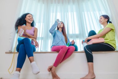 Çeşitli bayan arkadaş grupları antrenmandan sonra birlikte rahatlar, susuzluk çeker ve sohbet ederler. Yoga bloğu, direnç bandı ve egzersiz topuyla çevrili. Sağlıklı yaşam, dostluk, sağlıklı yaşam.