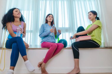 Çeşitli bayan arkadaş grupları antrenmandan sonra birlikte rahatlar, susuzluk çeker ve sohbet ederler. Yoga bloğu, direnç bandı ve egzersiz topuyla çevrili. Sağlıklı yaşam, dostluk, sağlıklı yaşam.