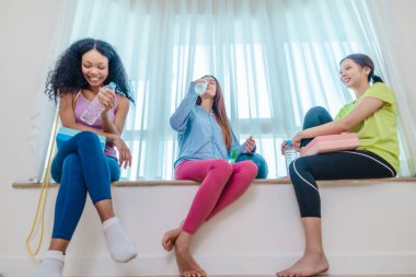 Çeşitli bayan arkadaş grupları antrenmandan sonra birlikte rahatlar, susuzluk çeker ve sohbet ederler. Yoga bloğu, direnç bandı ve egzersiz topuyla çevrili. Sağlıklı yaşam, dostluk, sağlıklı yaşam.