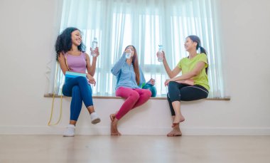 Çeşitli bayan arkadaş grupları antrenmandan sonra birlikte rahatlar, susuzluk çeker ve sohbet ederler. Yoga bloğu, direnç bandı ve egzersiz topuyla çevrili. Sağlıklı yaşam, dostluk, sağlıklı yaşam.