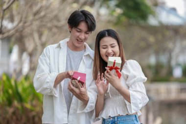 Asyalı bir çift, açık havada hediye kutularını değiş tokuş ederken neşeli bir anı paylaşıyor. Sahne, özel bir durum sırasında sevgi, kutlama ve bağlantı duygularını yakalar..