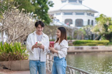 Asyalı bir çift, açık havada hediye kutularını değiş tokuş ederken neşeli bir anı paylaşıyor. Sahne, özel bir durum sırasında sevgi, kutlama ve bağlantı duygularını yakalar..