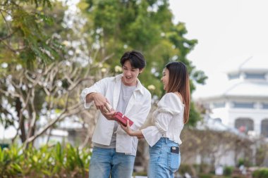 Asyalı bir çift, açık havada hediye kutularını değiş tokuş ederken neşeli bir anı paylaşıyor. Sahne, özel bir durum sırasında sevgi, kutlama ve bağlantı duygularını yakalar..