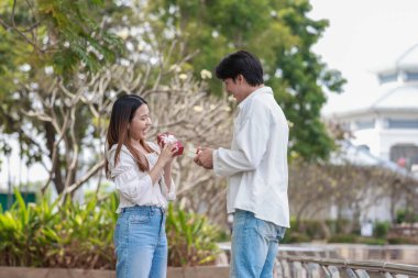 Asyalı bir çift, açık havada hediye kutularını değiş tokuş ederken neşeli bir anı paylaşıyor. Sahne, özel bir durum sırasında sevgi, kutlama ve bağlantı duygularını yakalar..