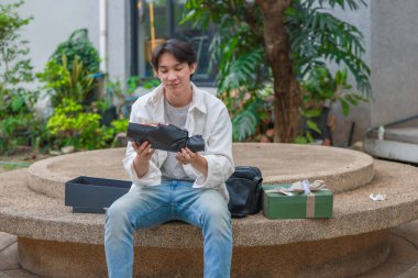 Asyalı bir adam elinde bir sürü hediye kutusu ve bir buket kırmızı gül tutarak sevinç ve heyecan ifade ederken sıcak bir şekilde gülümser. Romantik ve düşünceli bir jest yakalamak, kutlama için mükemmel..