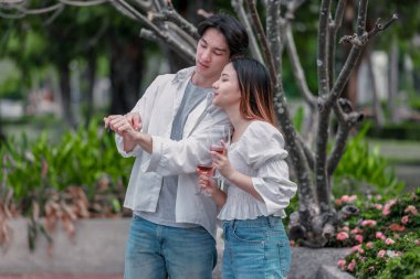 Asyalı çift kırmızı şarap ve sohbetten zevk alarak neşeli ve samimi bir anı paylaşıyor. Çiçekler ve yeşilliklerle çevrili. Romantizm, rahatlama ve bağlantı yakalamak