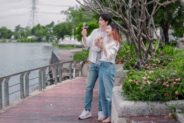 Asyalı çift kırmızı şarap ve sohbetten zevk alarak neşeli ve samimi bir anı paylaşıyor. Çiçekler ve yeşilliklerle çevrili. Romantizm, rahatlama ve bağlantı yakalamak