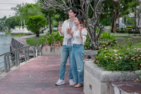 Asyalı çift kırmızı şarap ve sohbetten zevk alarak neşeli ve samimi bir anı paylaşıyor. Çiçekler ve yeşilliklerle çevrili. Romantizm, rahatlama ve bağlantı yakalamak