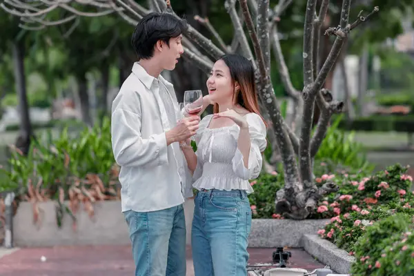 Asyalı çift kırmızı şarap ve sohbetten zevk alarak neşeli ve samimi bir anı paylaşıyor. Çiçekler ve yeşilliklerle çevrili. Romantizm, rahatlama ve bağlantı yakalamak