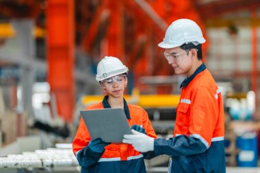 Güvenlik donanımlı iki metal levha fabrikası işçisi, bir endüstriyel ortamda proje yönetimi ve üretim geliştirme üzerinde yoğunlaşan bir dizüstü bilgisayarla stratejik bir tartışmaya girişti..