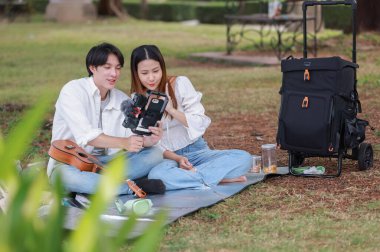 Asyalı çift piknik sırasında parkta dinlenmeyi, gülümsemeyi gitar çalmayı ve ukulele çalmayı seviyor. Doğal ortamda neşeli ve samimi bir bağlantı, müzik ve eğlence anı yakalıyorum..