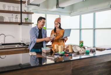 İki girişimci, modern bir çalışma alanında sürdürülebilir ambalaj örneklerini gözden geçiriyorlar. Çevre dostu materyaller ve ürün prototipleriyle çevrelenmiş olarak ürün geliştirme ve markalaşma fikirlerini tartışıyorlar.