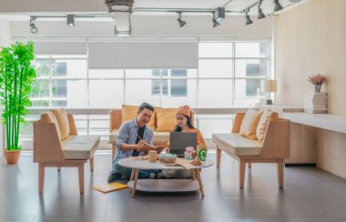 İki girişimci, modern bir çalışma alanında sürdürülebilir ambalaj örneklerini gözden geçiriyorlar. Çevre dostu materyaller ve ürün prototipleriyle çevrelenmiş olarak ürün geliştirme ve markalaşma fikirlerini tartışıyorlar.