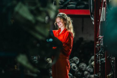 Kadın teknisyen depoda organize araba parçalarıyla dolu otomobil parçalarını elle inceliyor. Endüstriyel hassasiyet, yüksek hacimli otomotiv ayarlarında el işi.