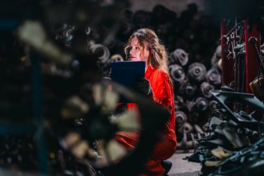 Kadın teknisyen depoda organize araba parçalarıyla dolu otomobil parçalarını elle inceliyor. Endüstriyel hassasiyet, yüksek hacimli otomotiv ayarlarında el işi.