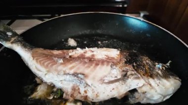 Yıldızlı bir restoranın şefi, yağlı ve baharatlı bir tavada balık fileto pişirir.