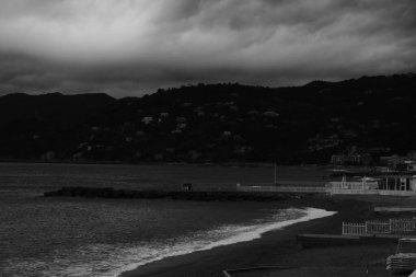 Deniz dalgalarının panoramik görüntüsü ve köpüğü koyu renklerle kumlu sahile çarpıyor.