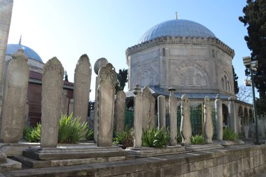 Güneşli bir günde cami kubbesinin önüne eski mezar taşları konur. 