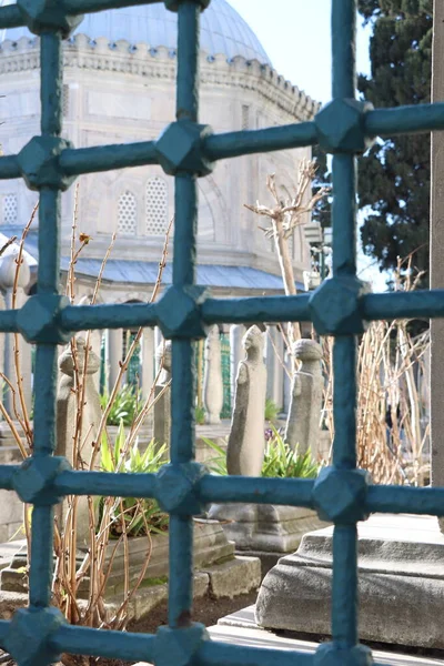 Mavi metal parmaklıkların arkasından görünen mezar taşları 