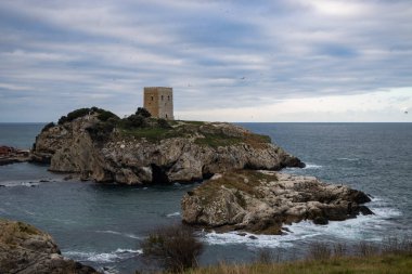Bulutlu bir günde etrafı suyla çevrili kayalık bir arazi.