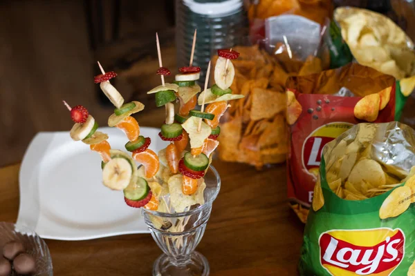 snack and fruit skewers placed next to chips on the snacks table 