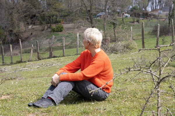 Sarışın bir kadın yerel bir çiftlikte çimlerde oturuyor.