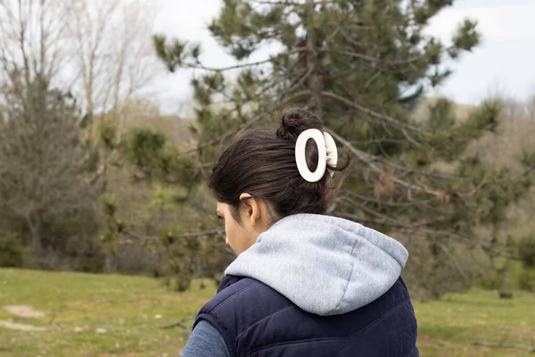 Beyaz saç tokalı bir kız. Arkasında ağaçlar ve çimenler olan yerel bir çiftliği keşfediyor.