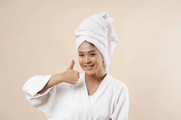 Portrait of a beautiful Asian woman on cream background closeup gesturing okay using her hand. Girl with clean skin. Isolated on a cream background.