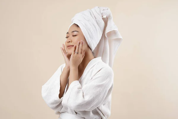 Portrait of a beautiful Asian woman on cream background closeup massaging her face. Girl with clean skin. Isolated on a cream background.
